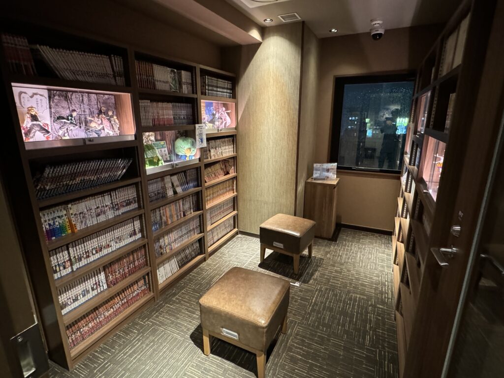 ドーミーイン池袋の漫画コーナー。スツールがあり落ち着いた雰囲気の書棚