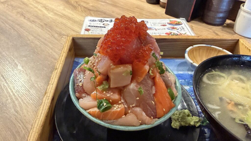 熱海おさかな・大食堂の看板メニュー「海鮮てっぺん丼」のアップ。マグロやサーモン、ブリなどの新鮮な地魚がタワー状に盛られ、頂上にイクラが散りばめられている