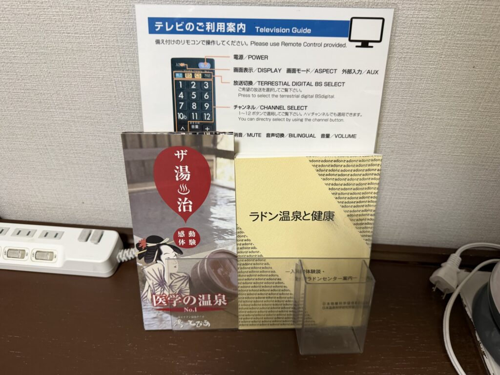 湯ーとぴあ客室に置かれたラドン温泉と健康の解説パンフレットとテレビ利用案内