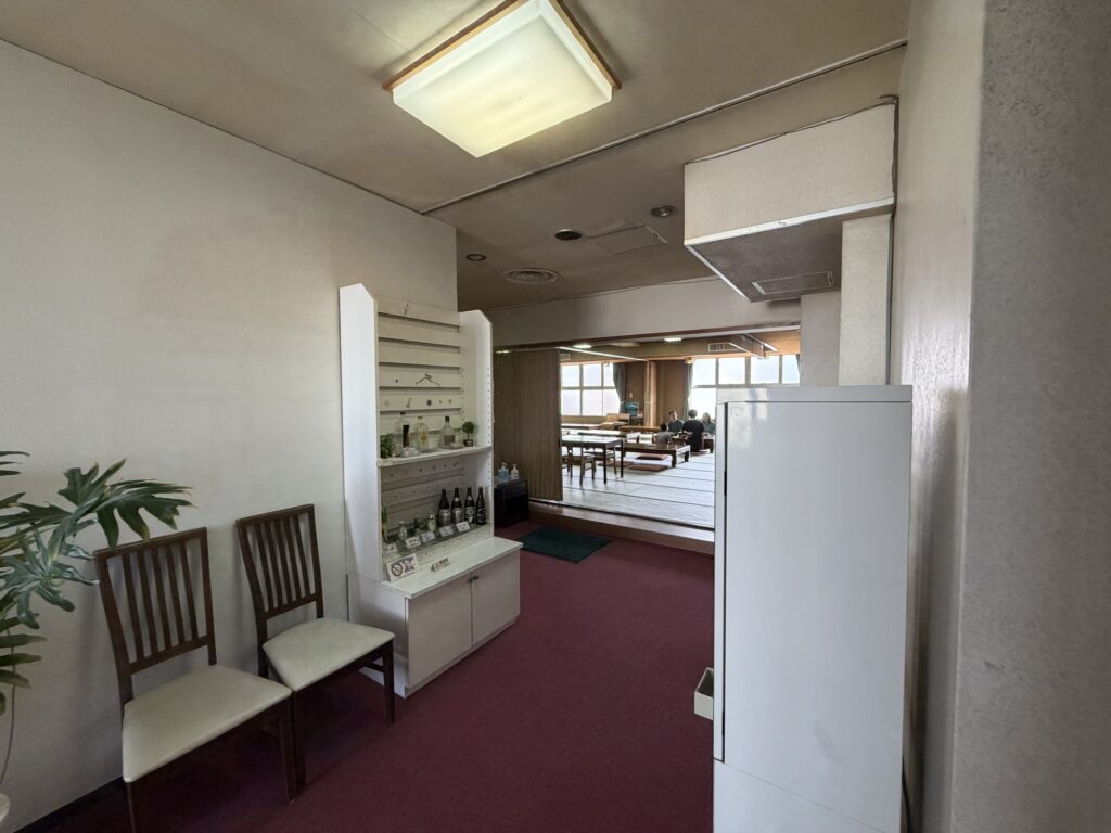 湯ーとぴあ2階の食事処へ続く通路 待合用の椅子と奥に見える和室の会場