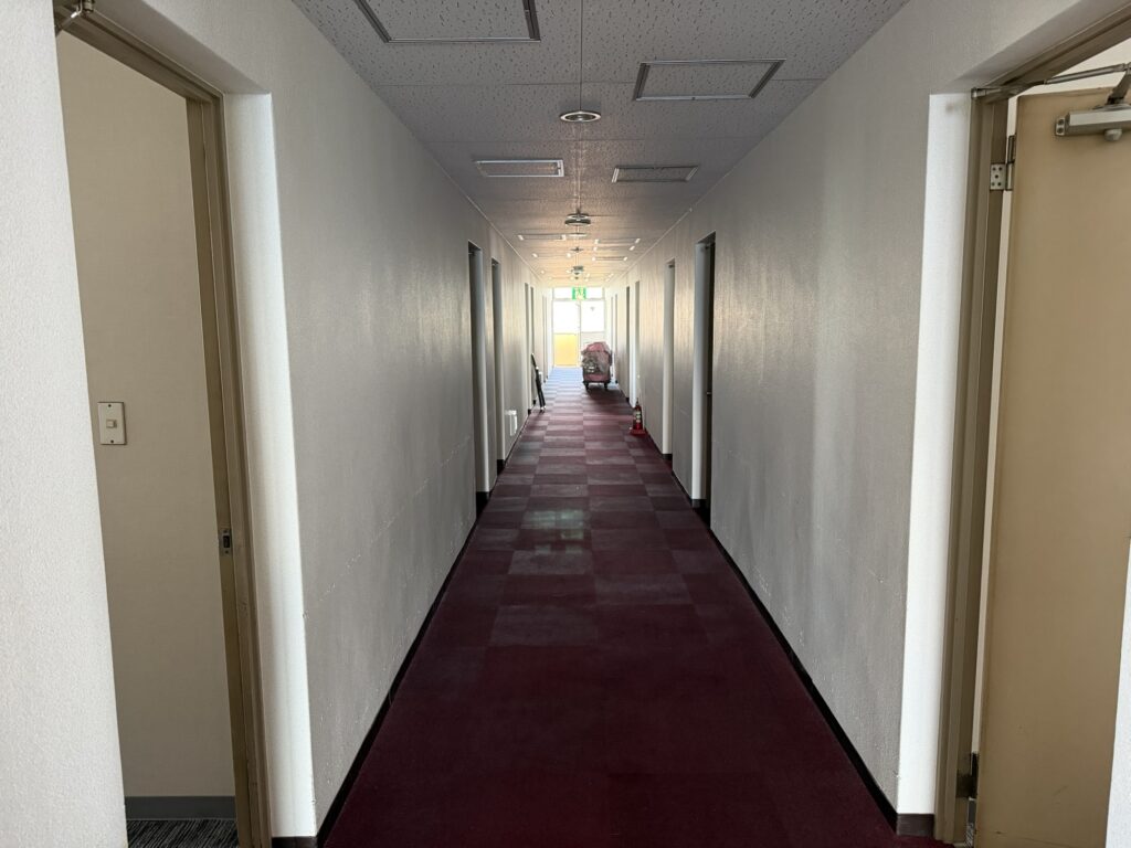 湯ーとぴあの客室階の廊下 えんじ色の絨毯がまっすぐ奥まで続く